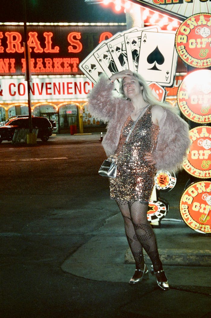 Woman in sequined dress posing near Las Vegas casino at night, vibrant lights.